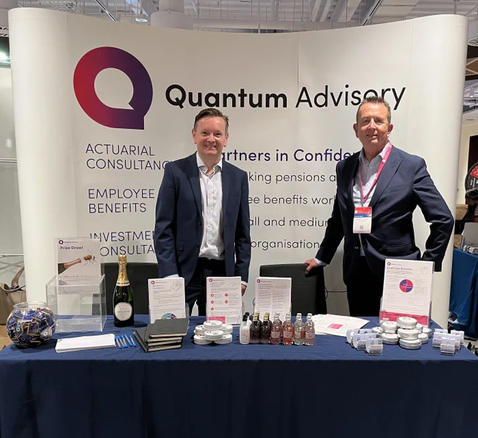Stuart and Graham at a conference in front of a branded Quantum Advisory banner and behind a table with merchandise and leaflets
