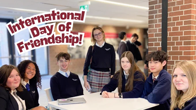 The visual contains the text "International Day of Friendship!" and seven smiling students sitting and standing around a table in a common space.