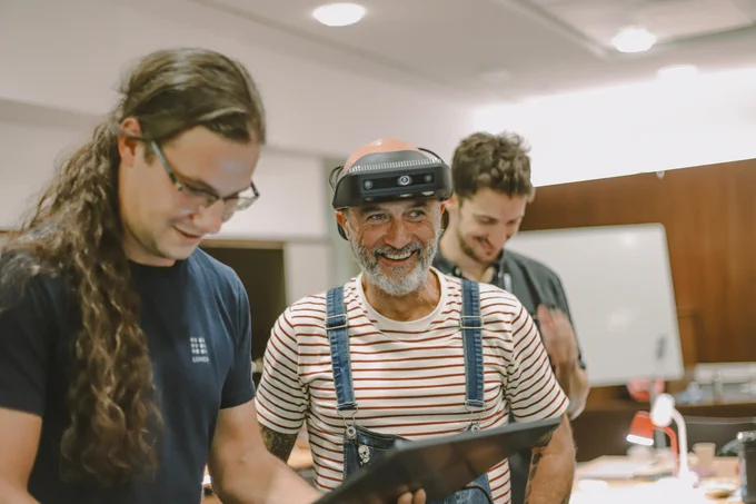 Three men are testing .lumen glasses in a room. The man in the center, wearing a striped shirt and overalls, is smiling while wearing the .lumen glasses. The man on the left, wearing a .lumen t-shirt, is holding a tablet and looking at it. Another man in the background is also smiling while watching the interaction. ​

Text on image: ​

Looking back on thousands of tests, there were lots of smiles and looots of fails. ​

We’ve done around 100,000 experiments. Probably around 97,000 failed. ​

That’s 97,000 ways we learned what not to do.​

Innovation happens through perseverance.​

​