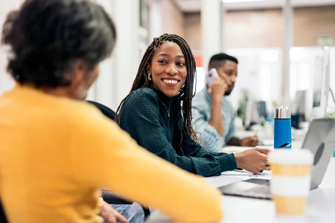 Female student sits with her peers at a table with laptops 