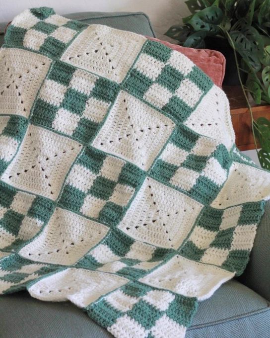 Green and white crocheted blanket with alternating solid and checkerboard square patterns draped over a gray couch.