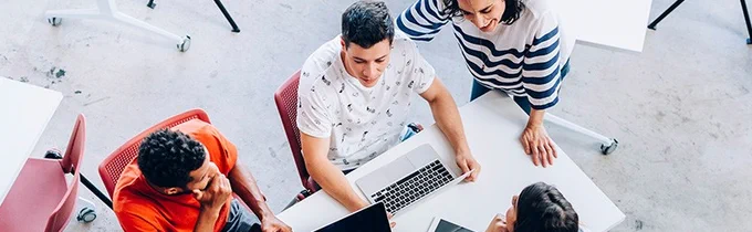 Menschen in lockerer Businesskleidung sitzen  vor ihren Labtops an einem Besprechungstisch und sprechen miteinander; Foto: istock / iStock-Cesar-Okada