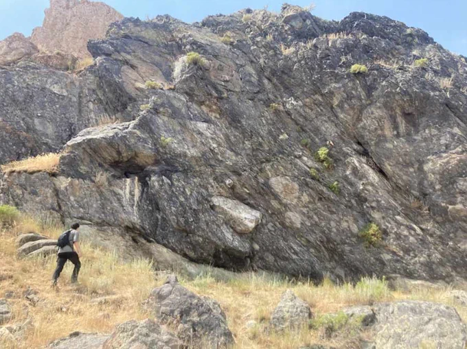 A person walks by a large rocky outcrop in a rugged terrain.