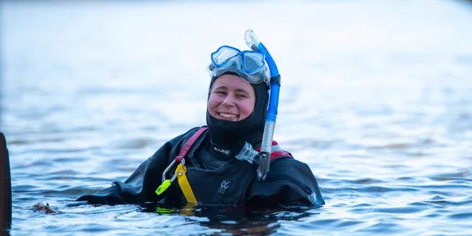UNBC student researcher in wetsuit smiling in water, equipped with a mask and snorkel.