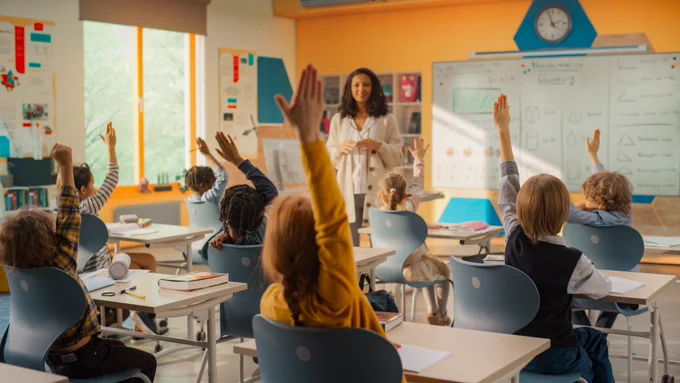 Elementary Classroom with Diverse Children Listening to the Teacher Asking a Question. Everyone Raising Hands in Order to Provide a Correct Answer. 