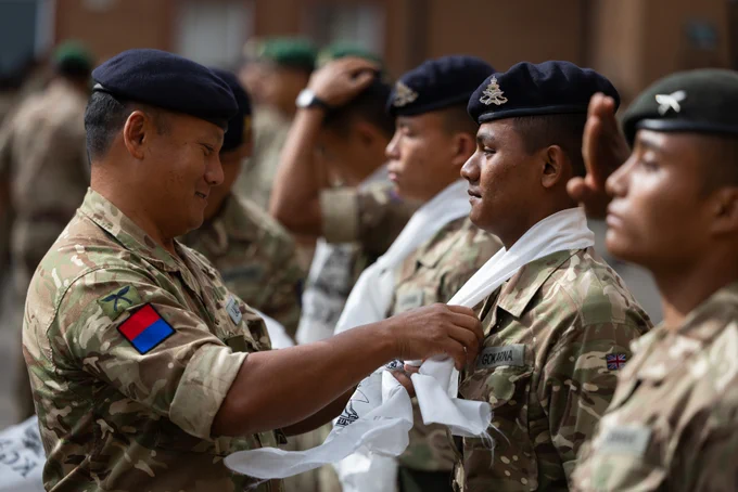 A British Army officer is tying a white scarf around the neck of a soldier.