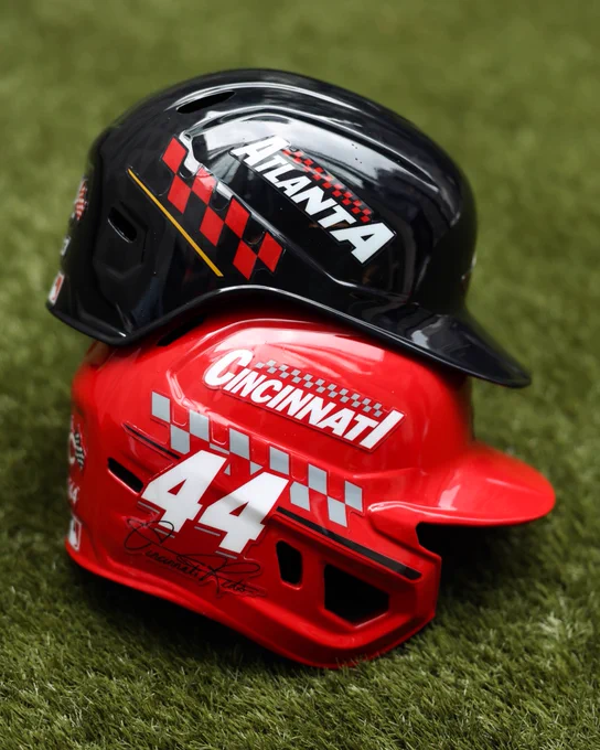 Braves and Reds Speedway Classic batting helmets positioned on top of each other on a grass area.