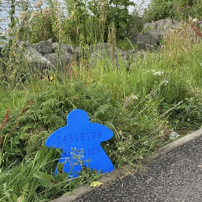 Giant meeple amongst the grass, with the caption Tabletop Scotland on it.