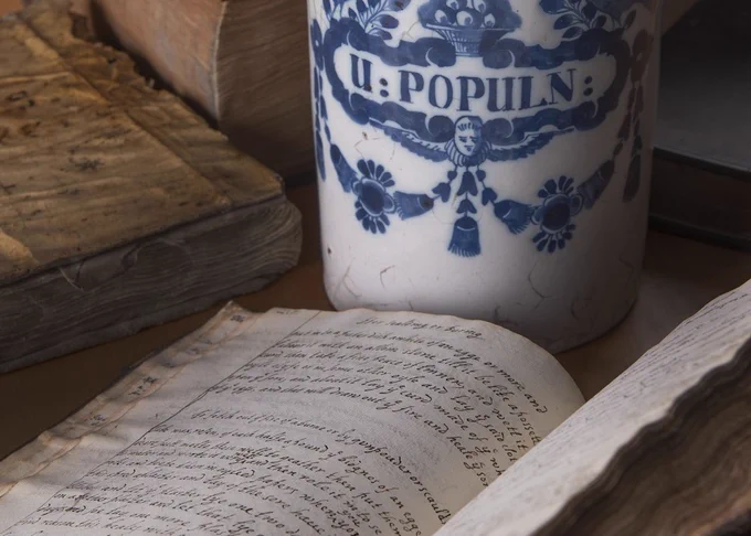 A blue and white ceramic apothecary jar with an open handwritten recipe book in front.