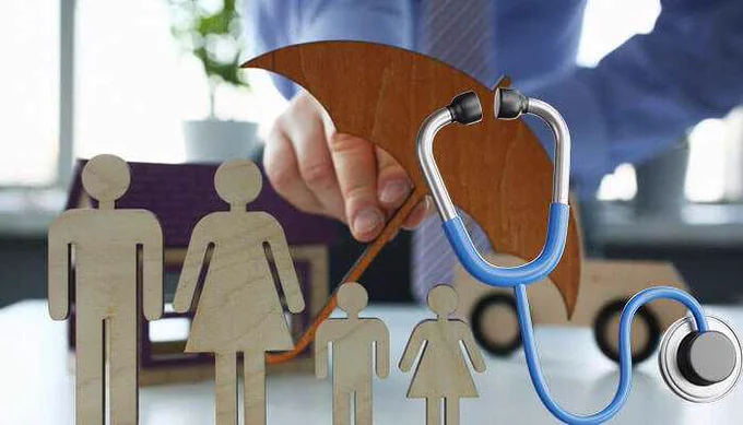 A stethoscope and umbrella covering a wooden cutout family symbolizing protection, representing the concepts of life insurance and health insurance for family well-being and financial security.