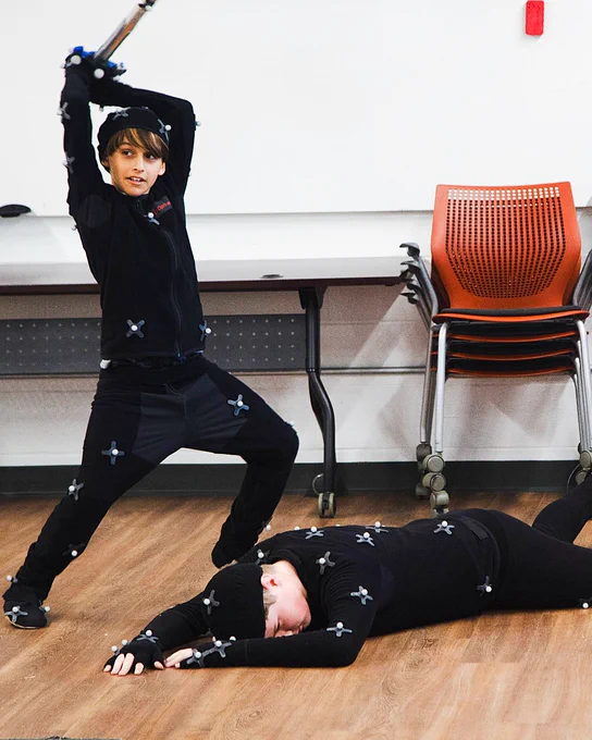 Two students act out a sword fight scene in motion capture suits.