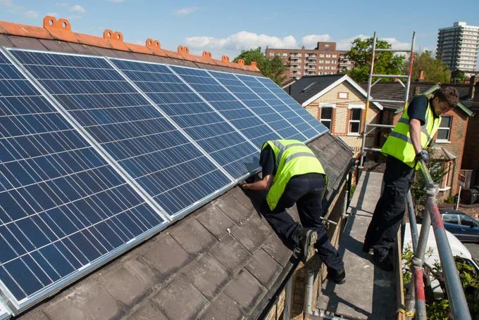 Two men in high vis jackets are pictured installing solar panels on a slate roof.