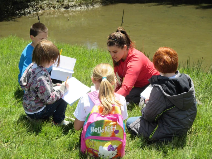 A teacher leads an outdoor education session next to the water.