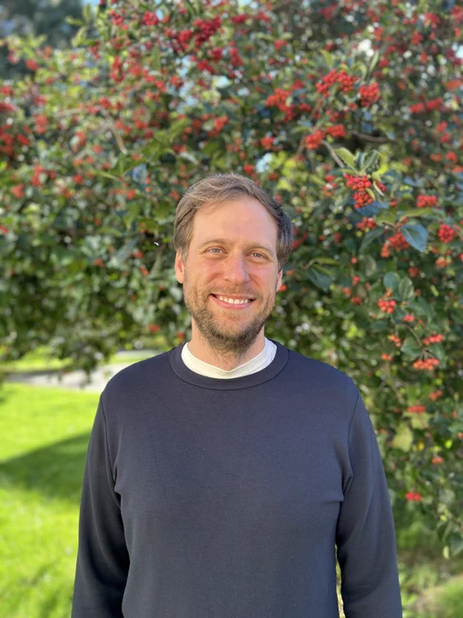 First author Christian Kofoed, a former postedoc in the Muir Lab, standing outside with a flowering tree behind him. 