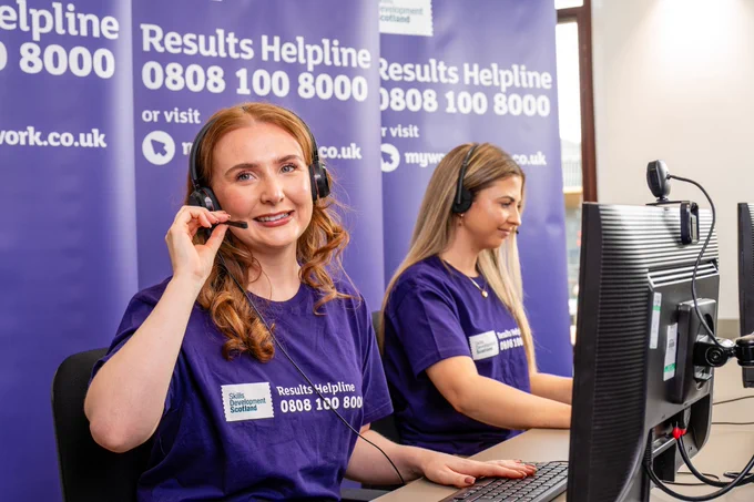 Two helpline advisers at phone desks with Results Helpline branding behind. 