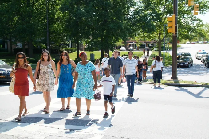 Families walking through a park on a sunny day, with trees and grassy areas in the background