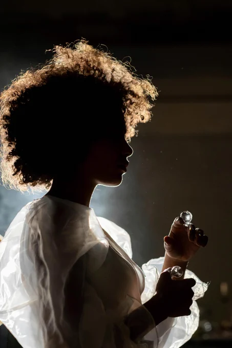 Una mujer negra a contraluz, que lleva un vestido vaporoso y juega con unas esferas de cristal.