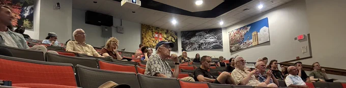 a crowd of seated, attentive people listen in a university lecture hall