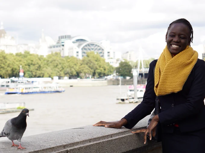 Effie stands beside a pigeon on the Southbank smiling, the North bank visible.