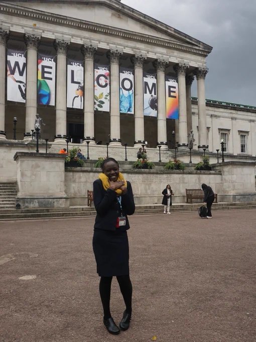 Effie stands in front of UCL's Portico building on campus, which has a colourful "Welcome" banner.
