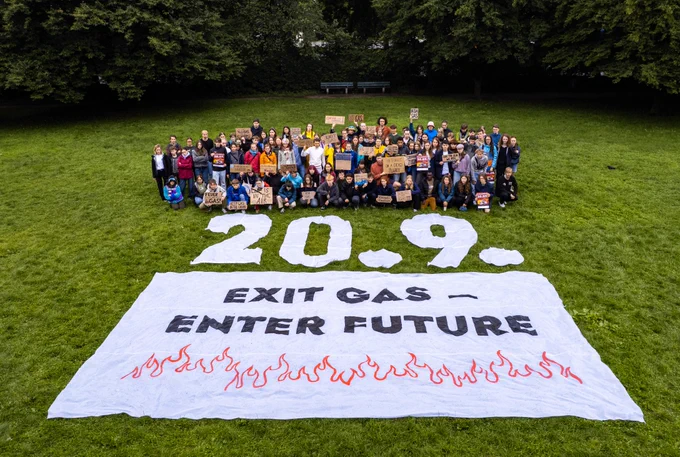 Menschen mit Pappschildern auf einer Wiese, davor die Zahlen 20.09. Und der Schriftzug Exit Gas Enter Future auf einem Banner
