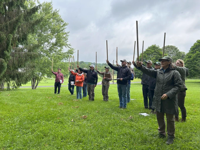 Group of middle-aged people standing in a field holding Biltmore sticks in the air. 