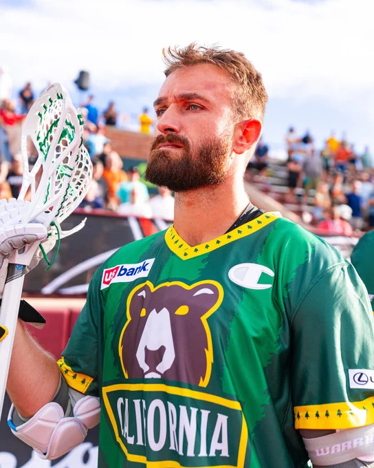 A California Redwoods lacrosse player in a green jersey holding a lacrosse stick on the field.