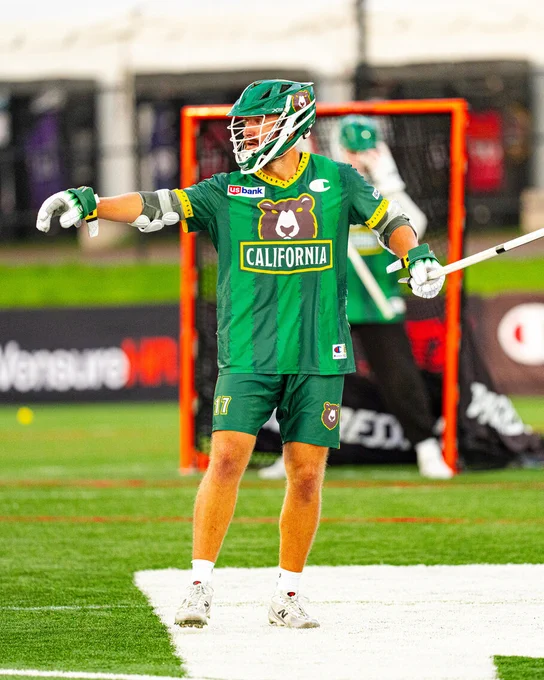 A Redwoods lacrosse player in a green and yellow California team uniform holding a lacrosse stick on the field.