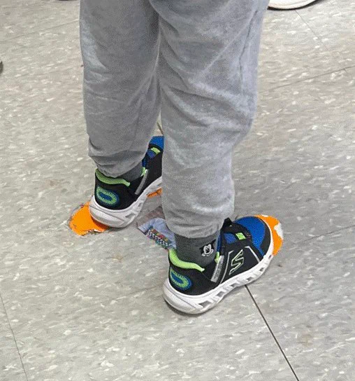 student standing on orange footprints taped to the floor as a visual cue of where to stand in line