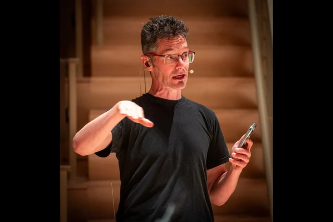 Eran Egozy, wearing a head-mounted microphone and holding a cellphone, addresses an unseen audience. He is guiding them in the use of their cell phones during the performance of his piece, “EV6.” Photo: Jonathan Sachs
