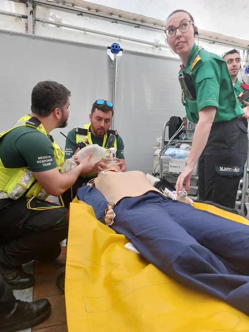 MRT members manually ventilating a manikin while Dr Pool speaks to another SJA volunteer off-screen. They are in the treatment centre, a brightly-lit gazebo.