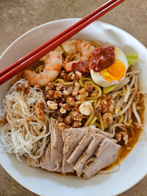 Dinner as described served in a white bowl. A pair of red chopsticks lie on a diagonal atop the plate.