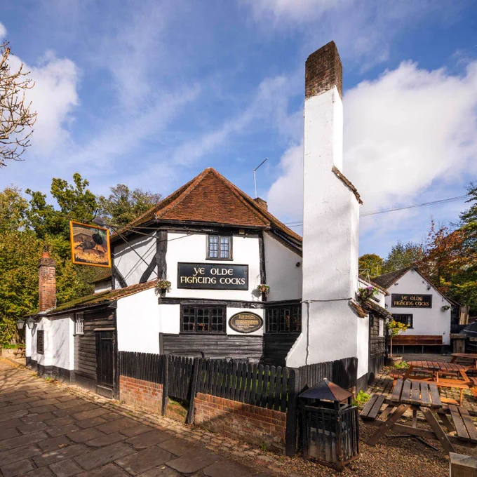 A photograph of the exterior of a timber-framed, old pub beside a small pub garden.