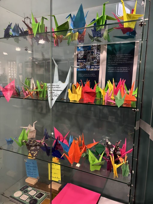 Images of brightly coloured paper cranes in a display cabinet with messages of peace. 