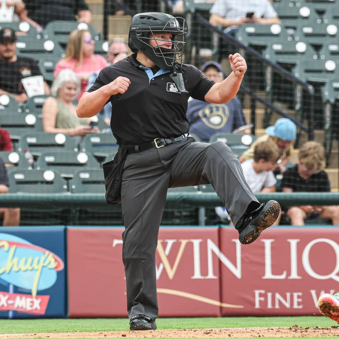Jen Pawol makes a strikeout motion while wearing an all black umpire uniform