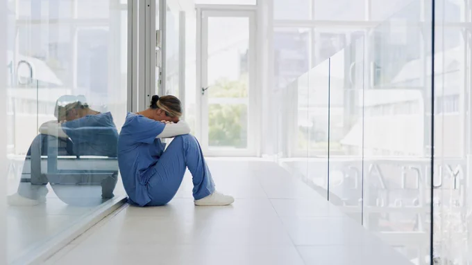 A clinician sitting in a hallway with their head on their knees. 