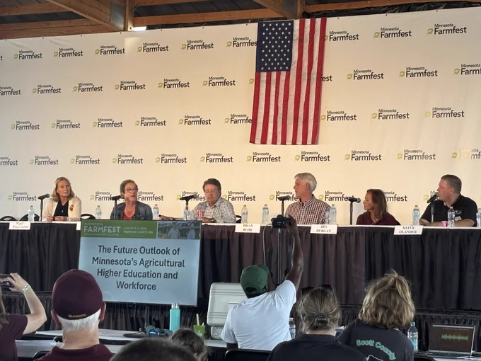Dean Bev Durgan on a panel of higher ed leaders seated at a table with an American flag displayed above.