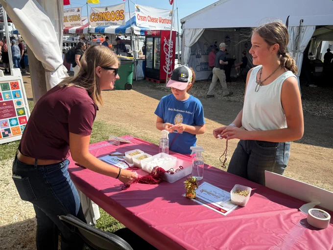 Two young Farmfest attendees chat with an Extension educator at a table.