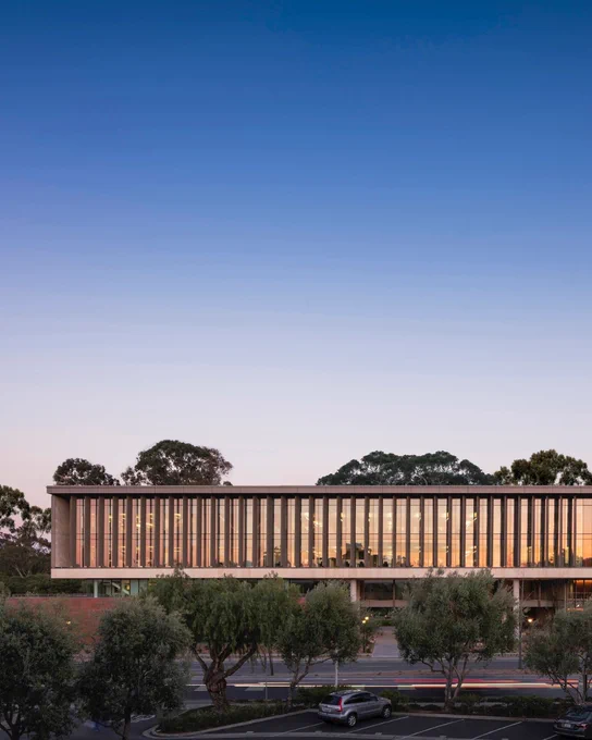 Exterior view during twilight, featuring its unique, translucent marble paneled facade illuminated from within, with surrounding trees and parked cars.