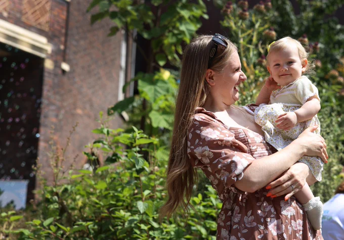 A Women wearing brown flower dress holding baby in a summer garden.