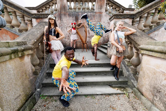 Dancers and musicians posing dynamically on an ornate outdoor staircase, dressed in eclectic and colorful outfits.