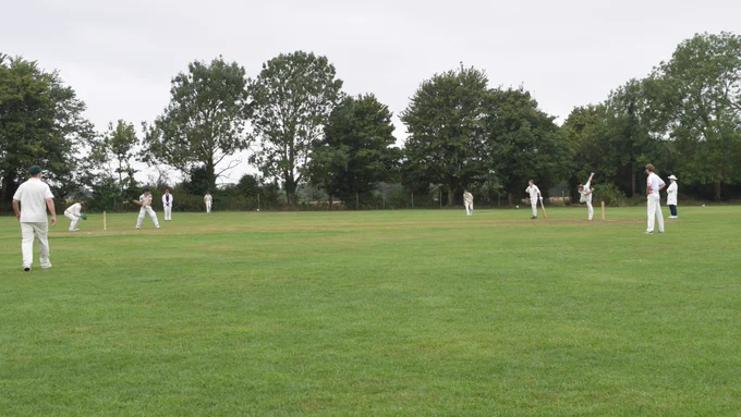 View from boundary shows keeper, slip, point and other fielders watching on as batter tries to hit ball as umpire looks on