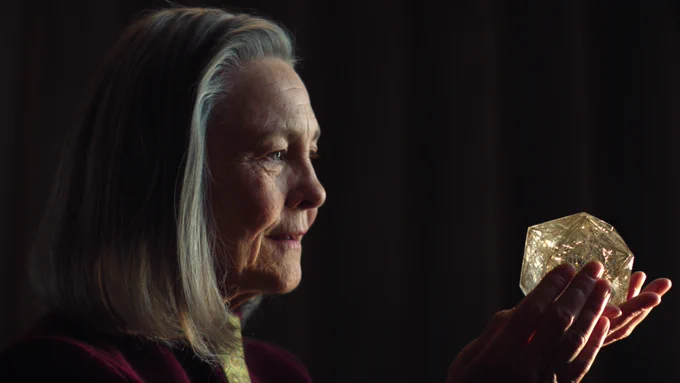 Cherry Jones as Ambassador Quent holds the Prime Radiant up to her face, examining it closely.