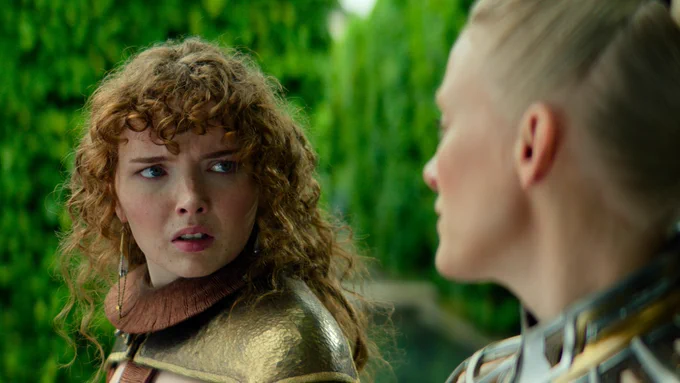 Laura Birn as Demerzel sits facing Rebecca Ineson as Zephyr Vorellis, who has a concerned expression, in a lush green garden.