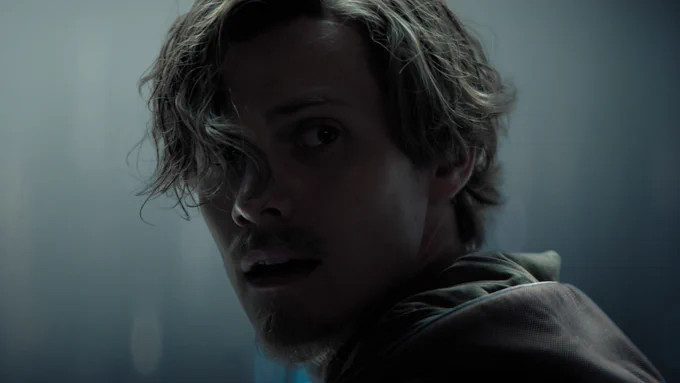 A close up of Cassian Bilton as Brother Dawn looking backward in a dark and moody tunnel.
