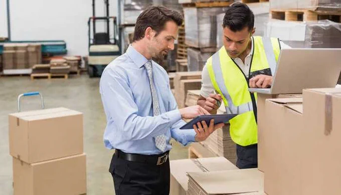 Logistics managers discussing package details in a warehouse during the pre-shipment process – illustrating what Pre Shipment mean in supply chain.