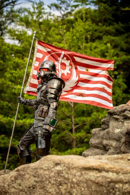 A person in a full Brotherhood of Steel Recon Armor set, holding a placed Brotherhood of Steel flag