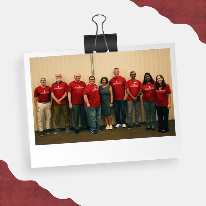 Group of nine individuals standing in a row wearing red shirts posing for a photo.