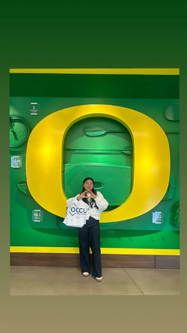 Person standing in front of a large yellow letter 'O' at an Oregon Ducks facility, throwing the O with their hands.