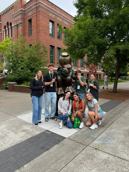 Group of people posing with the University of Oregon Duck mascot statue on campus.